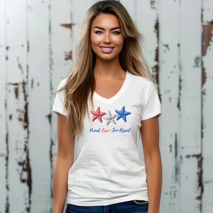 Smiling girl against a whitewashed wooden wall wearing White V-neck T-shirt with red, white, and blue starfish and the phrase "Proud, Free & Sun-Kissed" printed on the front.