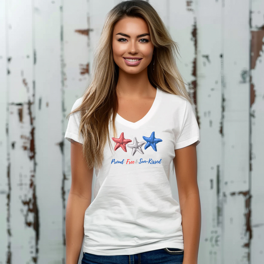 Smiling girl against a whitewashed wooden wall wearing White V-neck T-shirt with red, white, and blue starfish and the phrase "Proud, Free & Sun-Kissed" printed on the front.