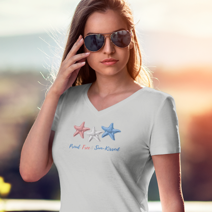 Girl in sunglasses with outdoor blurred backdrop wearing a Gray V-neck T-shirt with red, white, and blue starfish and the phrase "Proud, Free & Sun-Kissed" printed on the front.
