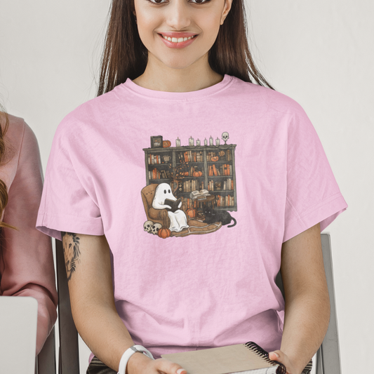 Person wearing a pink t-shirt with a graphic design of a ghost, cat, and books.