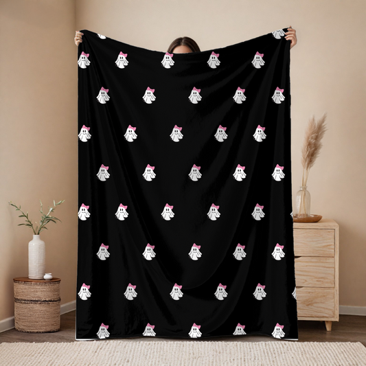 Person holding a black blanket with white ghost patterns in a room.