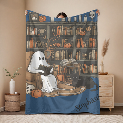 Person holding a Halloween-themed blanket with ghost, cat, and bookshelf design.