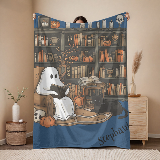 Person holding a Halloween-themed blanket with ghost, cat, and bookshelf design.