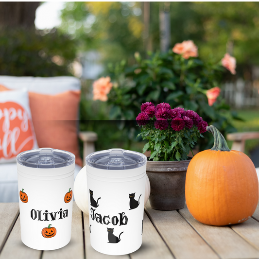 Two personalized tumblers with names 'Olivia' and 'Jacob', a pumpkin, and potted plant on a wooden surface outdoors.