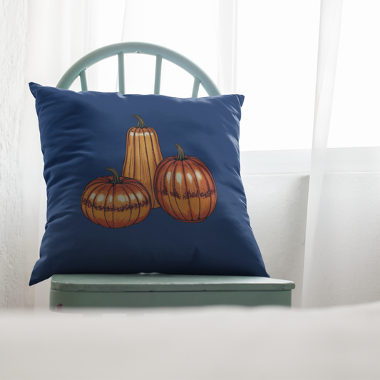 Blue square pillow with a rustic pumpkin trio illustration, placed on a light green chair near a sunlit window, creating a cozy fall aesthetic.

