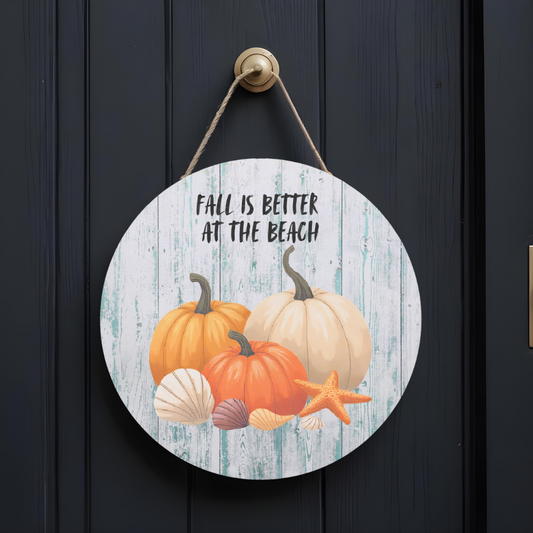 Round wooden sign with pumpkins, seashells, and a starfish on a beach-themed design, hanging on a dark wooden door.