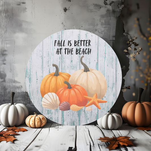 Decorative sign with pumpkins and text 'Fall is better at the beach' on a rustic wooden background.