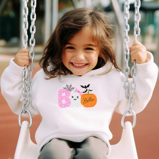 Child on a swing wearing a white sweatshirt with Halloween-themed designs.