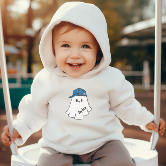 Child wearing a white hoodie with a ghost design, sitting on a swing outdoors.