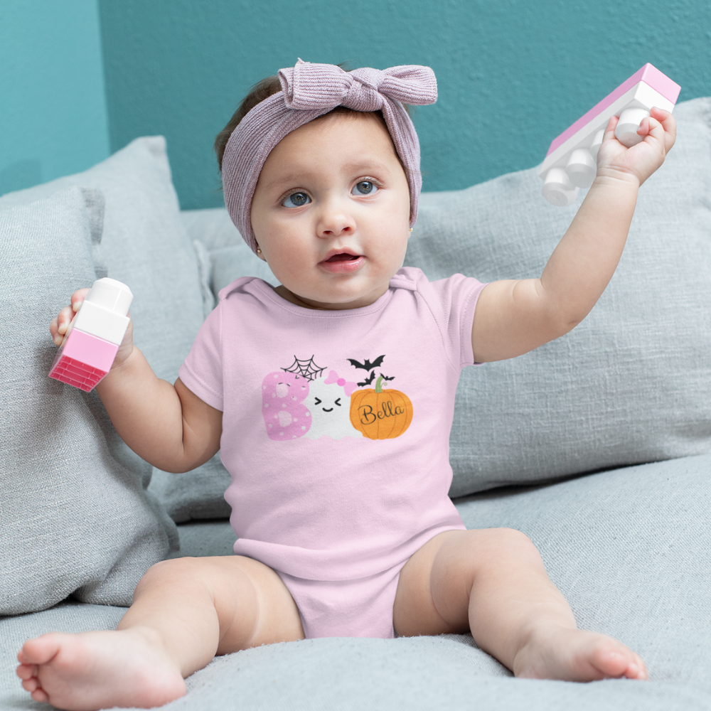 Baby in a pink onesie with a bow sitting on a gray couch.