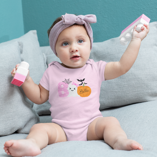 Baby in a pink onesie with a bow sitting on a gray couch.