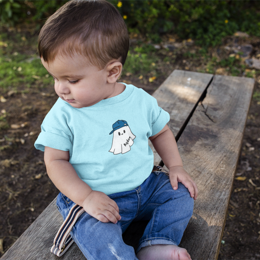 Child wearing a light blue t-shirt with a ghost design sitting on a wooden bench outdoors.