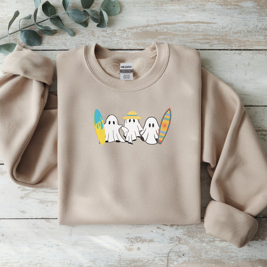 Beige sweatshirt with cartoon ghosts and surfboards on a wooden surface