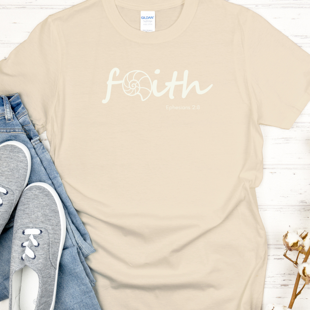 Beige t-shirt with 'faith' printed on it, paired with jeans and sneakers on a light wooden surface.