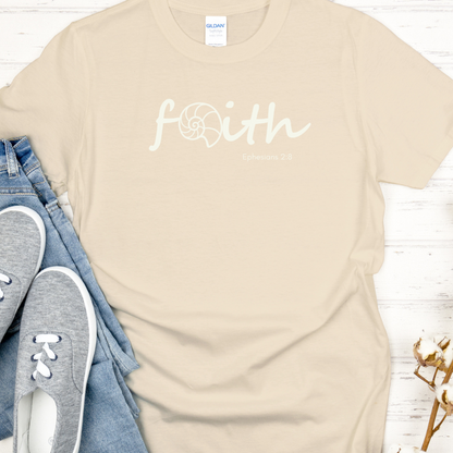 Beige t-shirt with 'faith' printed on it, paired with jeans and sneakers on a light wooden surface.