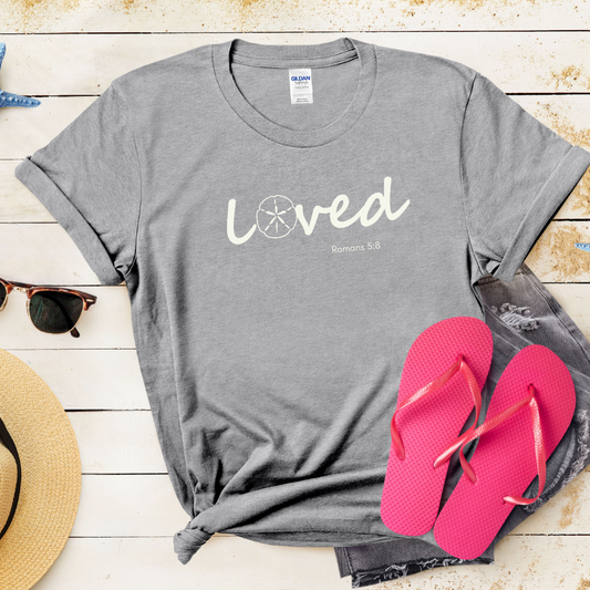 Gray t-shirt with 'LOVED' text, pink flip-flops, and sunglasses on a wooden surface