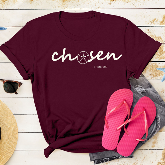 Maroon t-shirt with 'chosen' text, pink flip-flops, and sunglasses on a wooden surface