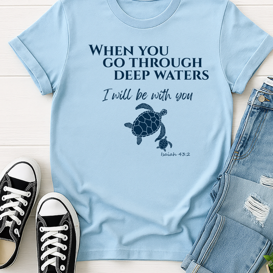 Light blue t-shirt with turtle graphic and text, paired with black sneakers and jeans on a light wooden surface.