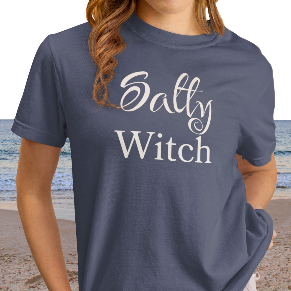 Person wearing a blue t-shirt with 'Salty Witch' text on a beach.