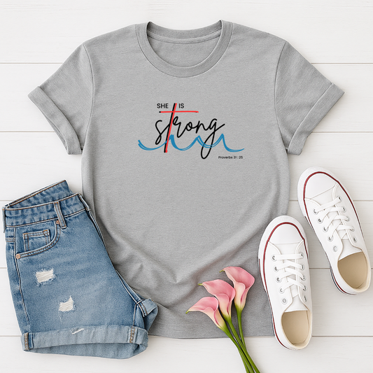 Gray t-shirt with 'She is Strong' text, paired with denim shorts, white sneakers, and pink flowers on a light wooden surface.