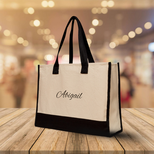 Beige tote bag with black handles and trim on a wooden surface with a blurred background