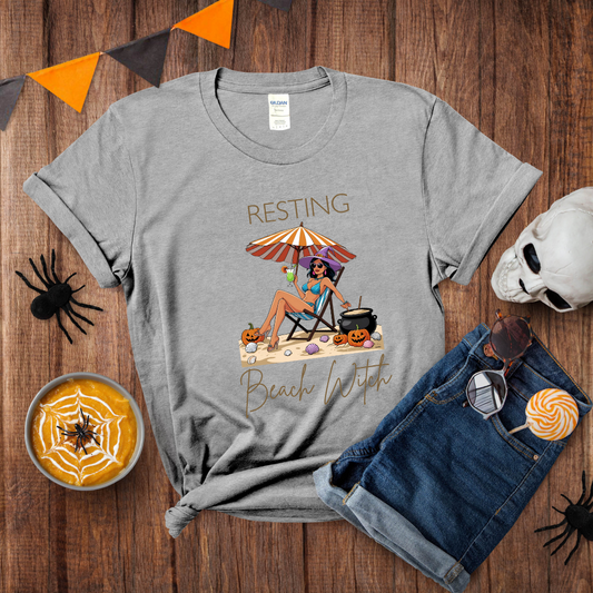 Gray t-shirt with 'Resting Beach Witch' design on a wooden surface with Halloween decorations.