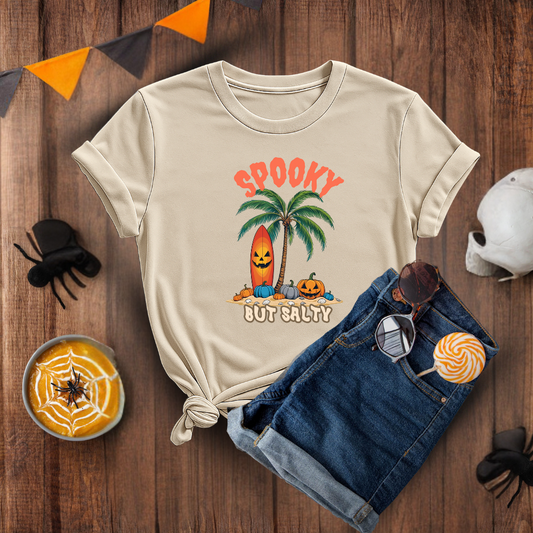 Beige t-shirt with Halloween-themed design on a wooden surface with accessories.