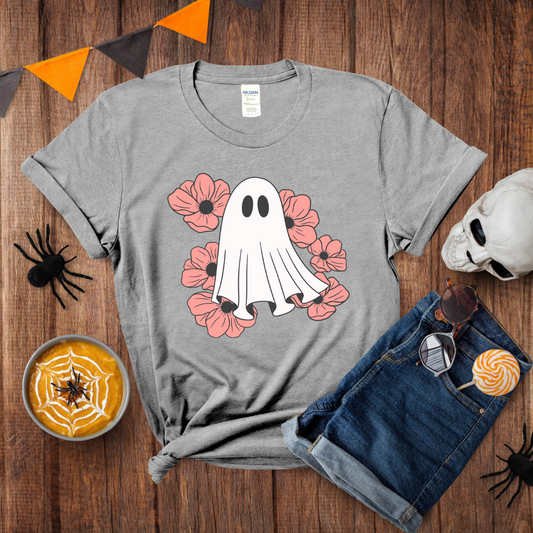 Gray t-shirt with a ghost and flower design on a wooden surface with Halloween decorations.