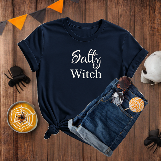 Navy blue t-shirt with 'Salty Witch' text on a wooden surface with Halloween-themed items.