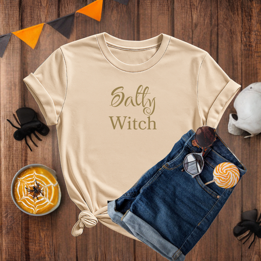Beige t-shirt with 'Salty Witch' text on a wooden surface with Halloween-themed items.