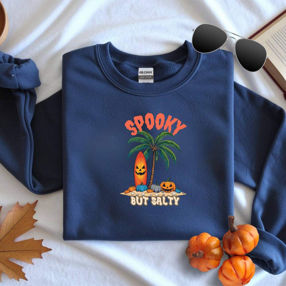 Folded navy blue sweatshirt with Halloween-themed design on a white surface with pumpkins and leaves.