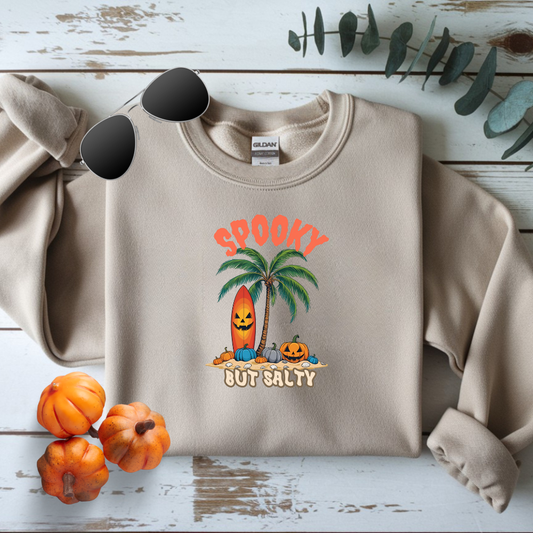Beige sweatshirt with Halloween-themed design featuring a palm tree and pumpkins on a wooden surface.