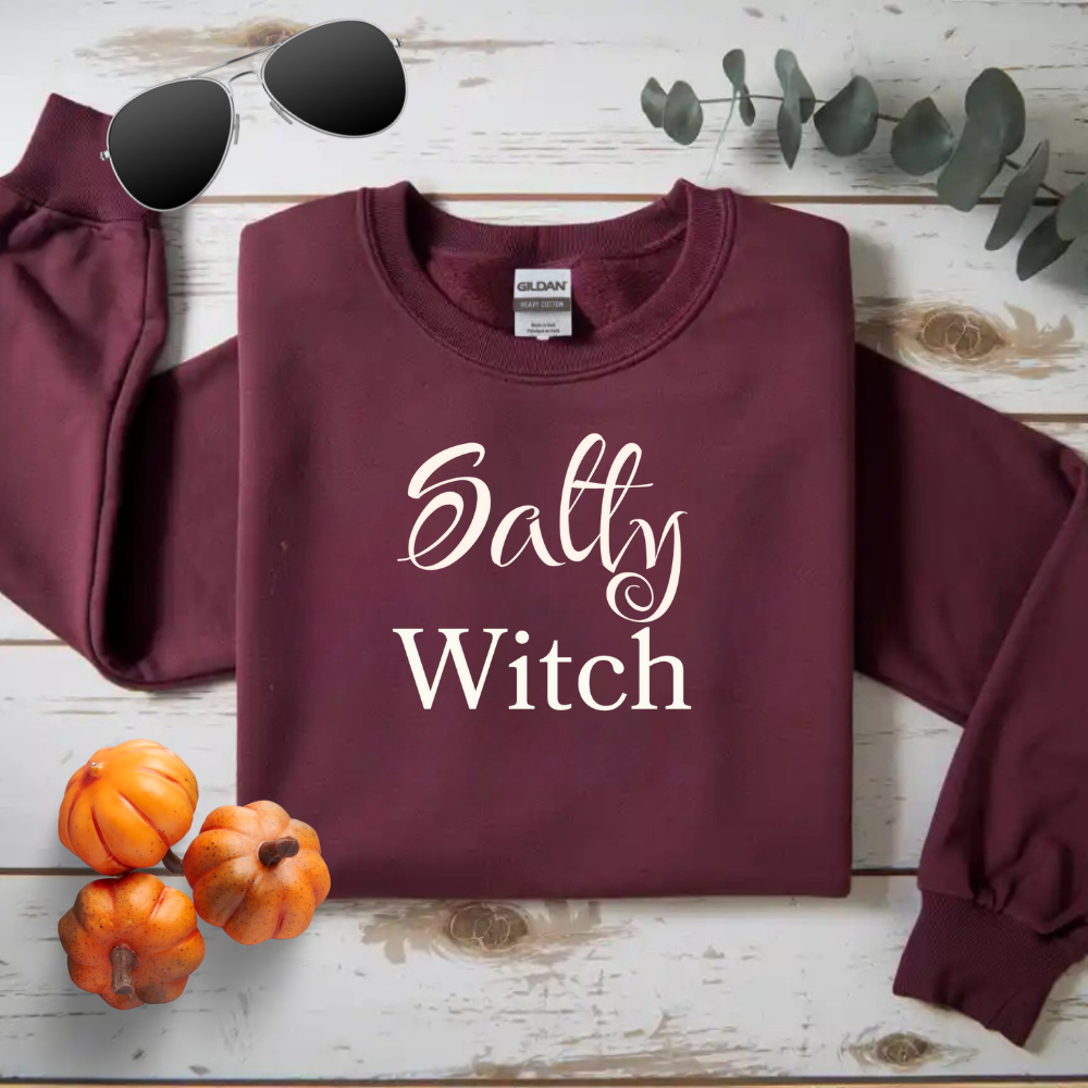 Maroon sweatshirt with 'Salty Witch' text on a wooden surface with pumpkins and sunglasses.
