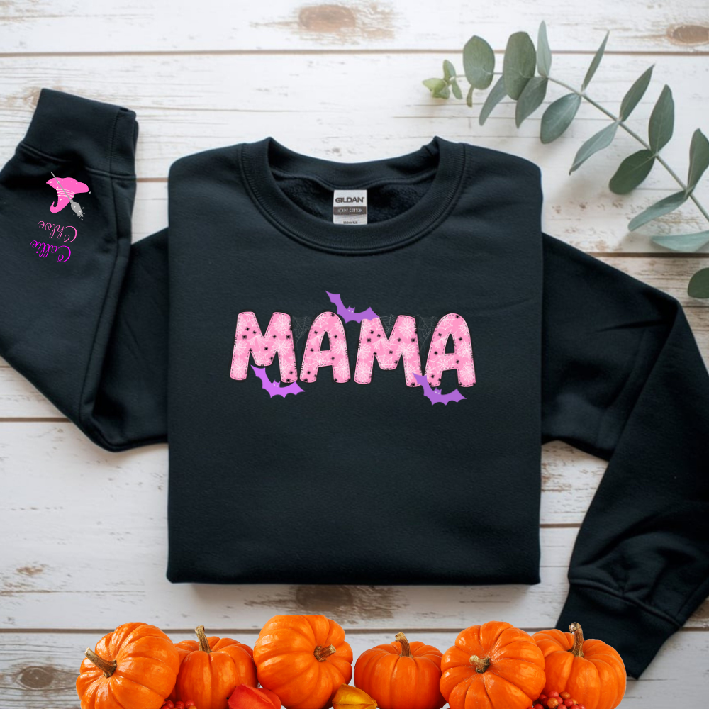 Black sweatshirt with 'MAMA' text on a wooden surface with pumpkins and leaves.