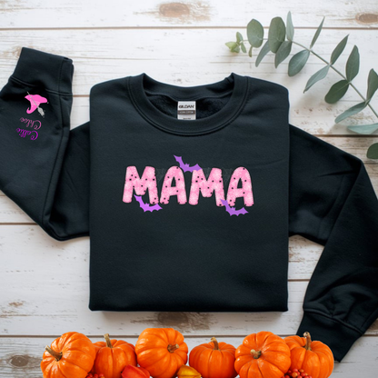 Black sweatshirt with 'MAMA' text on a wooden surface with pumpkins and leaves.