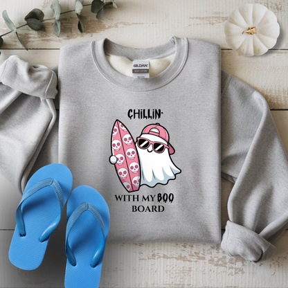 Gray sweatshirt with a ghost and surfboard graphic and blue flip-flops on a wooden surface.