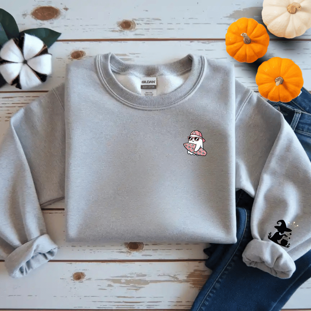 Gray sweatshirt with a small design on a wooden surface with pumpkins and decorative items.