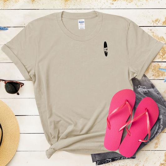 Beige t-shirt with a small graphic, pink flip-flops, and a straw hat on a wooden surface.