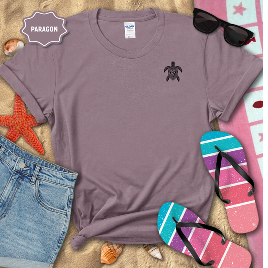Purple t-shirt with a turtle design on a sandy surface with beach accessories.