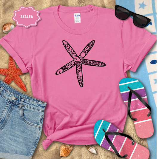 Pink t-shirt with a starfish design, sunglasses, and flip-flops on a sandy background.