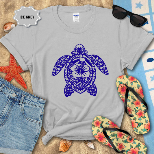 Gray t-shirt with a blue turtle design on a sandy background with beach accessories.