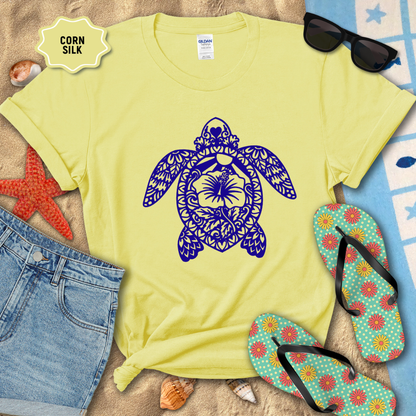 Yellow t-shirt with a blue turtle design on a sandy surface with flip-flops and sunglasses.