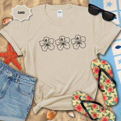 Beige t-shirt with floral designs on a sandy background with flip-flops and sunglasses.