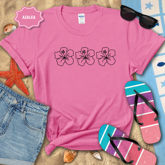 Pink t-shirt with floral design on a beach setting with sunglasses, flip-flops, and denim shorts.