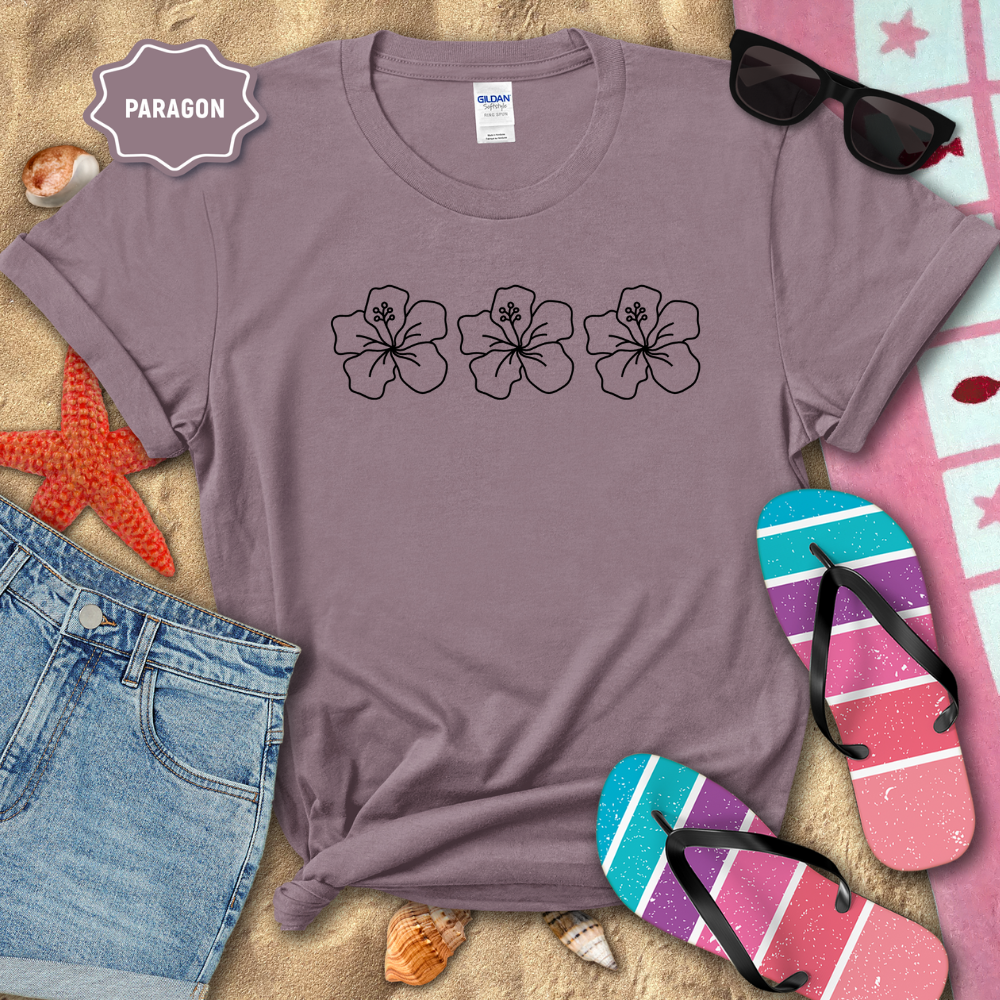 Purple t-shirt with floral designs on a sandy surface with beach accessories.