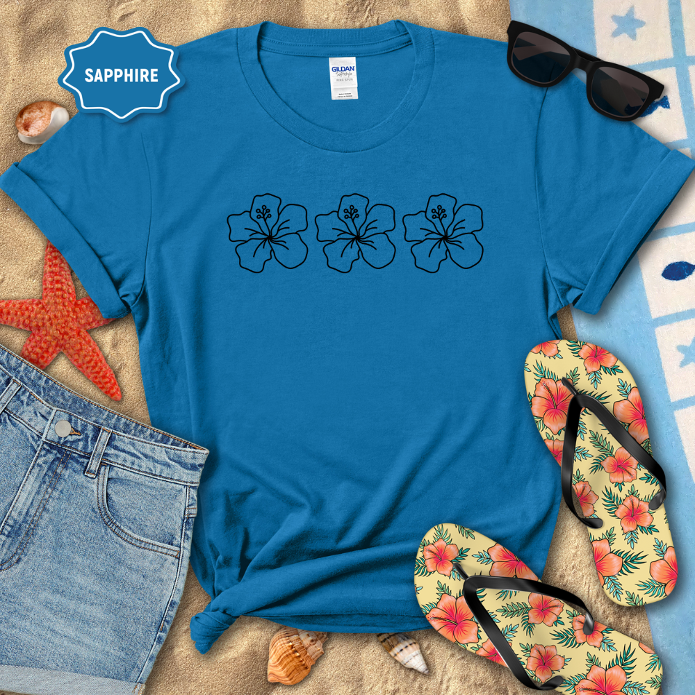 Blue t-shirt with floral designs on a beach setting with sunglasses, flip-flops, and denim shorts.