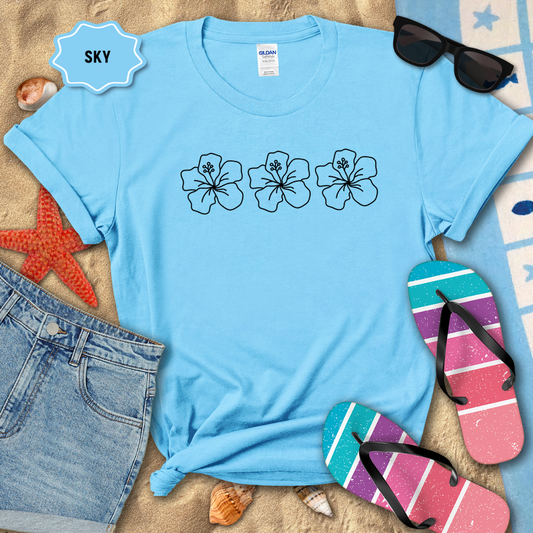 Blue t-shirt with floral designs on a sandy surface with beach accessories.