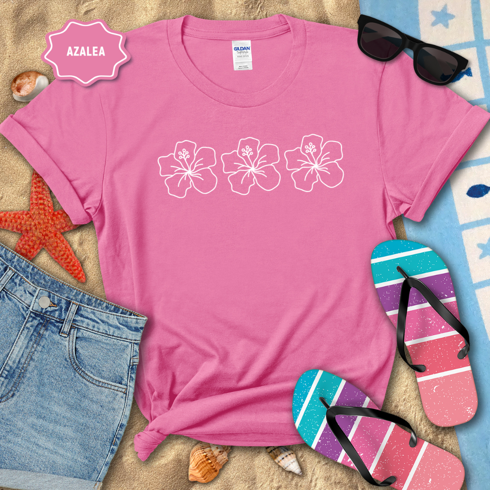 Pink t-shirt with white floral designs on a beach-themed background with sunglasses, flip-flops, and denim shorts.