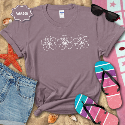Purple t-shirt with floral designs on a sandy surface with beach accessories.