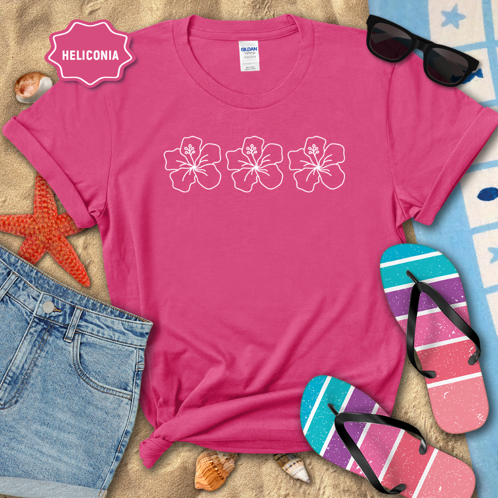 Pink t-shirt with floral design on a sandy surface with sunglasses, flip-flops, and denim shorts.